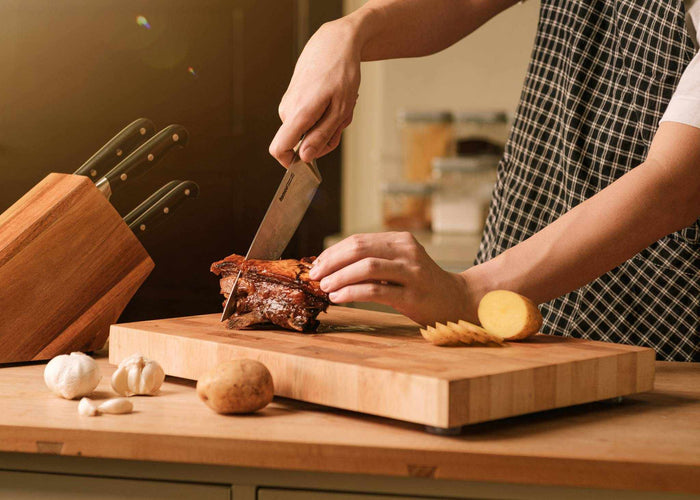chef knife slicing meat on a maple wood chopping board