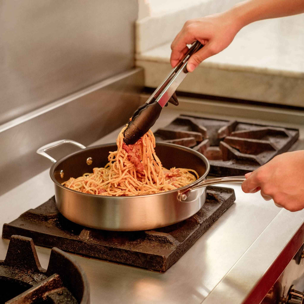 picking up pasta using kitchen tongs on a non stick saute pan
